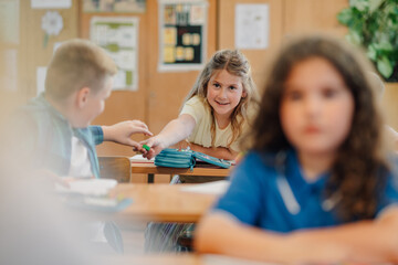 Girl student sharing crayon with classmate in elementary school classroom