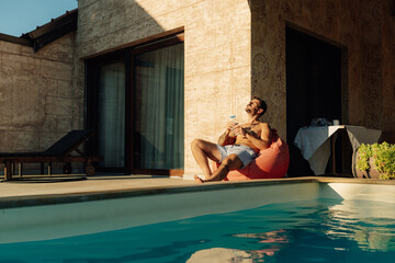 Man relaxing by the poolside of luxury villa, enjoying a refreshing drink