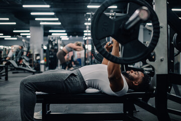 Determined male athlete lifting weights while bench pressing in gym