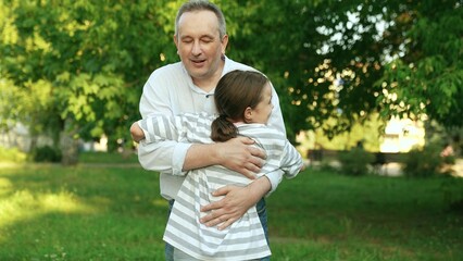 Fototapeta premium Dad meets little daughter in park family hug. Little daughter runs to her father in park hugs him. Concept of happy family. Family nature walk in summer. Family people together. Daughter love dad