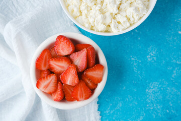 bowl of cottage cheese and sliced strawberries on blue textured background