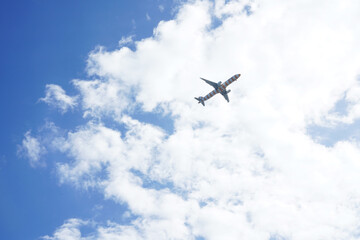 A plane is soaring high through a vast, cloudy blue sky above