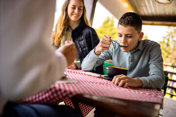 Teenage kids having lunch with their parents on the terrace of a mountain restaurant during a sunny spring or autumn day.