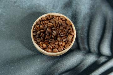 Coffee beans in wooden bowl with leaf shadow on dark background