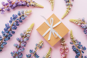 Gift box and lupin flowers on pink background with space for text