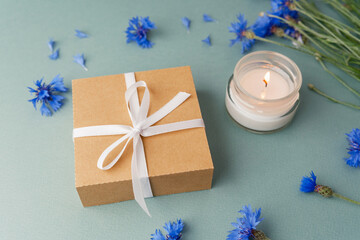 Gift box with candle and cornflowers on green background