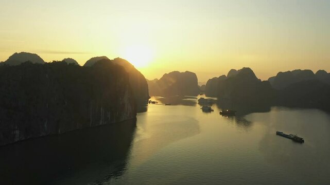 Cargo ships navigating calm waters amidst towering limestone karsts during a breathtaking golden sunrise in Ha Long Bay