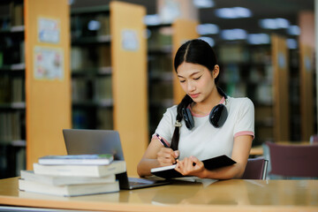 Fototapeta premium A dedicated female student spends her free time calmly researching in the library, wearing headphones and enjoying music while focusing on her studies.