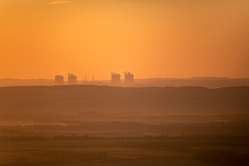 Dukovany Nuclear Power Plant at sunset with steam rising from cooling towers, set in a scenic landscape. Perfect for energy, industry, and environmental themes.