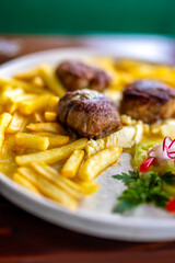 Juicy meatballs served with golden French fries on a white plate.