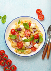 Plate with Italian fusilli pasta salad with fresh cherry tomatoes, mozzarella, olives, red onion, and basil leaves, concept of Italian culinary tradition