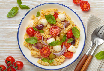 Plate with Italian fusilli pasta salad with fresh cherry tomatoes, mozzarella, olives, red onion, and basil leaves, concept of Italian culinary tradition