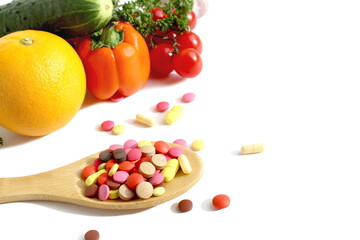 On a white background lies a wooden spoon with medicine and in the background are vegetables and fruits.	