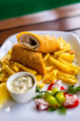 Breaded rolled meat served with crispy French fries on a white plate.