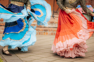 Close-up of dancers in traditional, colorful layered skirts during a lively folk performance,...