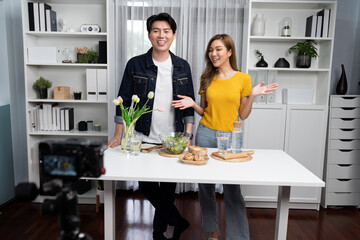 Cooking show on live streaming with two chef influencers teaching mixed salad with dressing for easy special recording on video camera. Ingredients placing bread bun wholegrain side dish. Infobahn.