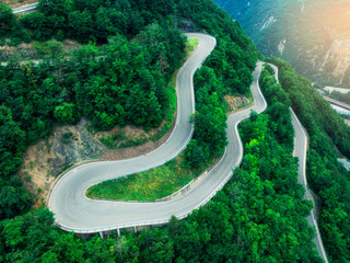 Aerial view of mountain curvy road and green forest in summer. Dolomites, Italy. Top drone view of winding road on mountain pass, trees in spring. Road through the woods. Moody landscape with roadway