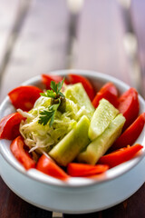 Fresh cucumber and tomato salad served in a bowl on a wooden table.