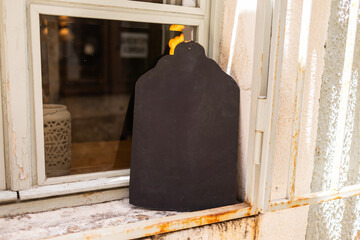 Blank chalkboard sign on windowsill in rustic setting. Outdoor signage, vintage decor, and small...