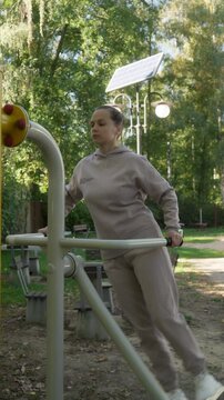 A woman works out her core muscles on an air swinger machine in an outdoor gym. This twisting, side-to-side motion targets the obliques and waist for a strength workout.