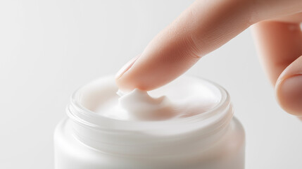Close-up of a finger touching a jar of white skincare cream.
