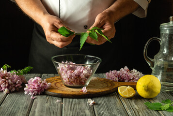 Adding green mint to a glass container with acacia flowers before making cold and aromatic kvass. Concept of folk medicine or making a healthy drink