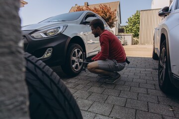 Man changing car tire on roadside using tools, vehicle lifted on jack. Concept of auto repair, maintenance, breakdown assistance and real-life situations
