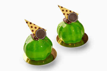 Two shiny green mousse cakes with chocolate decorations and gold substrates