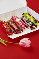 Box of colorful eclairs with tulip on red background