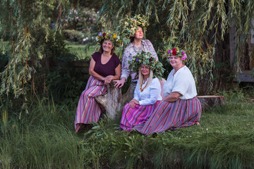 On the evening of the summer solstice, women show off their crowns and colorful clothes. Outdoors, on the shore by a body of water.