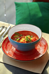 Tom yum soup served in blue bowl on red plate with cutlery aside