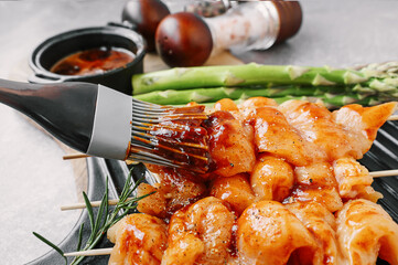Brush with marinade sauce for marinating kebabs. Raw chicken breast kebab. Raw sliced chicken breast on wooden sticks with asparagus