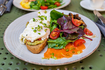 A healthy gourmet breakfast with poached eggs on avocado toast, salmon, and fresh salad