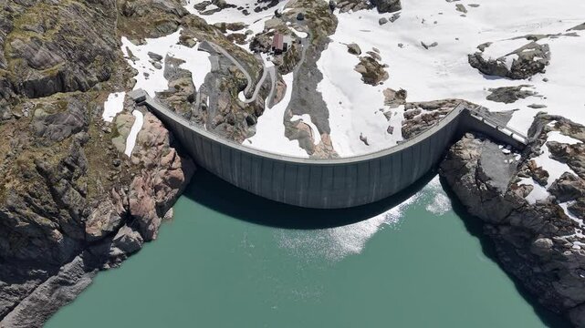 Vue a&eacute;rienne spectaculaire d&rsquo;un barrage en arc au c&oelig;ur des Alpes, entour&eacute; de neige et de montagnes rocheuses. Vid&eacute;o drone 4k 60fps
