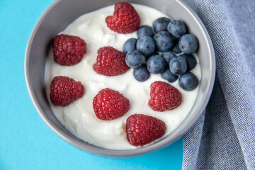 Gray bowl and natural yogurt with red berries on the blue background.