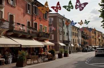 Via Giuseppe Garibaldi a Desenzano del Garda, decorata con farfalle sospese tra gli edifici colorati in stile veneziano, con una caffetteria accogliente sulla sinistra, durante un luminoso pomeriggio 