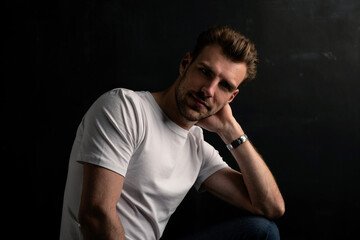 Portait of a young man sitting against isolated dark background