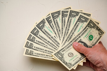Hand holding various denominations of United States currency arranged fanned out against a light background