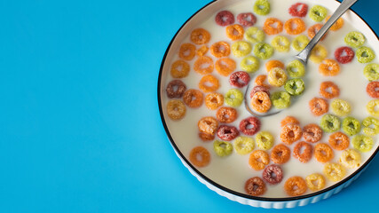 Colorful breakfast cereal in milk on blue background with spoon for morning meals. Copy space
