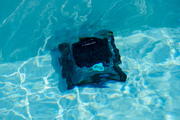 Robotic pool cleaner operates in clear blue water during sunny afternoon by the backyard pool