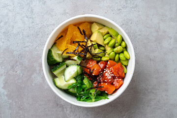 A vibrant salad bowl features slices of fresh salmon, crunchy cucumber, sweet orange segments, and tender edamame