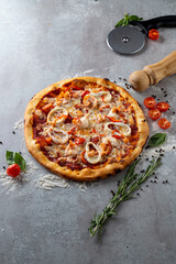 A vibrant pizza is beautifully arranged with slices of bell peppers, cherry tomatoes, and fresh herbs on a gray surface. Nearby, a rolling pin and pizza cutter add to the culinary atmosphere