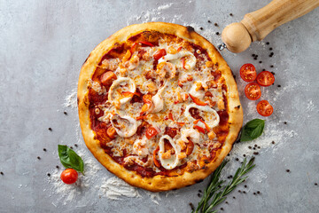 A mouthwatering pizza emerges from the oven, featuring succulent shrimp, vibrant red tomatoes, melted cheese, and aromatic fresh herbs, set against a textured gray backdrop