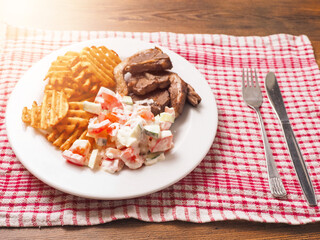 Dinner with fine lamb loin chops, potato lattice and fresh salad with sour cream on a white plate, red and white small towel, fork and knife. Fine meal made with popular ingredients.