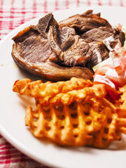 Dinner meal with cooked lamb loin chops, potato lattice and fresh salad with sour cream. Close up. Fine tasty dinner.