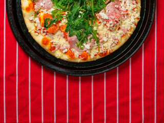 A pizza with ham and spinach on a black tray. The pizza is sitting on a red and white stripe table cloth. Fine Italian cuisine with fresh ingredients ready to be cooked. Fast food meal.