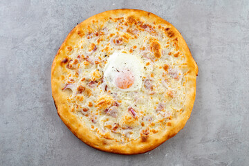 A delicious white pizza topped with a perfectly baked egg and fresh ingredients shines on a textured gray backdrop, tempting food lovers to experience its rich flavors and unique presentation