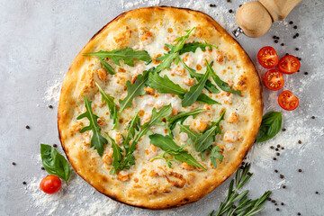 Mouthwatering white pizza garnished with tender shrimp and vibrant arugula sits elegantly on a rustic gray counter. Surrounding ingredients add to the culinary allure