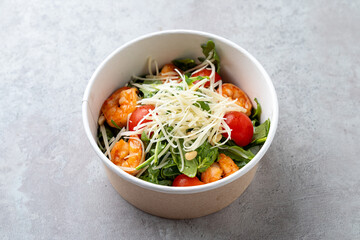 A vibrant bowl of shrimp salad features succulent shrimp, cherry tomatoes, and fresh greens topped with shreds of onion, showcasing a healthy and appetizing meal option