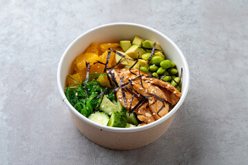 A vibrant bowl brimming with salmon, avocado, seaweed, and fresh vegetables sits against a sleek surface, inviting a delightful lunchtime experience with bright colors and textures